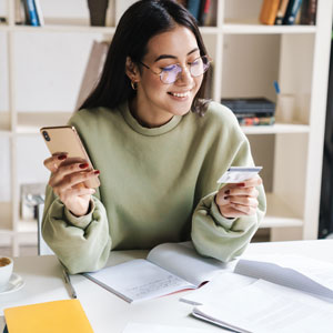 Young woman holding and looking at a credit card in her hand.